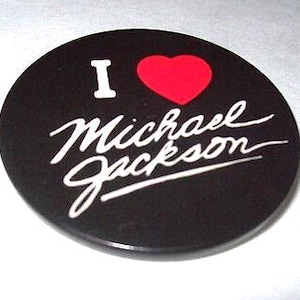May include: A round, black button with the text "I ❤️ Michael Jackson" in white script and a red heart. The button is a fan item, likely a collectible or accessory.