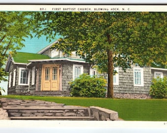 May include: Vintage postcard featuring the First Baptist Church in Blowing Rock, N.C. The church has a gray shingle exterior, a green roof, and a light yellow door. A stone staircase leads up to the church, surrounded by green grass and trees.
