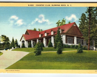 May include: A vintage postcard depicting a red-roofed country club building with stone accents. The building is surrounded by lush green grass and trees. The postcard is titled "N-622 Country Club, Blowing Rock, N.C."