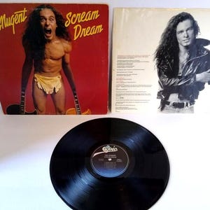 May include: A vinyl record album by Ted Nugent, titled "Scream Dream," featuring a red cover with a shirtless man holding guitars. The album is accompanied by a second album cover and a black vinyl record.
