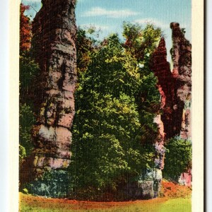 May include: Vintage postcard featuring Natural Chimneys near Mount Solon, Virginia. The image shows tall, weathered rock formations with lush green trees and grass. The sky is a light blue. Text on the card reads "V-614:-NATURAL CHIMNEYS. NEAR MOUNT SOLON, VIRGINIA."
