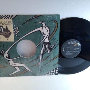 May include: A vinyl record and album cover for the song "Funky Town" by Pseudo Echo. The album cover is green with a white and black illustration. The record is black with an RCA label.