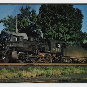 May include: A vintage postcard showing a black steam locomotive, numbered 1498, and a red caboose. The train is on tracks with green grass in the foreground, set against a backdrop of trees and a blue sky.