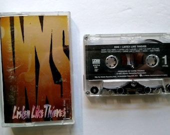 May include: A vintage cassette tape of the INXS album "Listen Like Thieves." The cassette case is clear, with the album art featuring a stylized orange and yellow design with the band's name. The cassette tape itself is visible, with song titles.