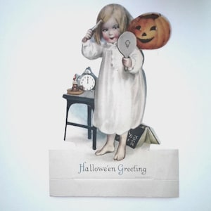 May include: A vintage die-cut paper greeting card featuring a child in a white nightgown holding a hand mirror and a hairbrush. Beside the child is a small black table with a clock, a pumpkin, and a book labeled Magic. Text reads Hallowe'en Greeting.