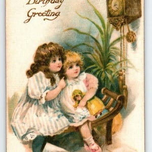 May include: Vintage birthday greeting card featuring two young girls in dresses, seated on a bench. A clock and greenery are in the background. The card has the words "A Birthday Greeting" in elegant script.