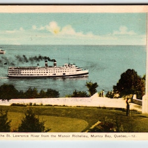 May include: A vintage postcard showing a large white passenger ship sailing on the water, with a smaller vessel in the distance. The scene is set against a blue sky and water, with green trees and a grassy area in the foreground. Text at the bottom reads: Overlooking the St. Lawrence River.