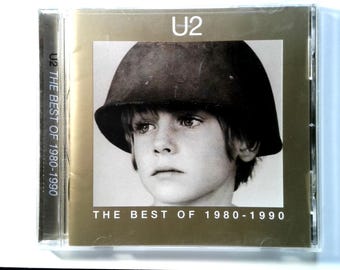 May include: U2's "The Best of 1980-1990" CD. The album cover features a black and white photo of a young person wearing a helmet. The band's name, U2, is at the top, and the album title is at the bottom.