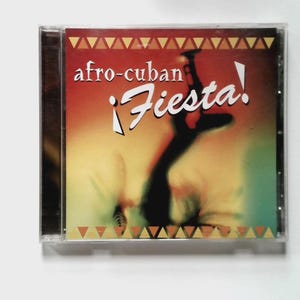 May include: CD case with the text "afro-cuban ¡Fiesta!" in white. The cover art features a silhouette of a dancer against a blurred orange and yellow background. The top and bottom of the cover have a repeating triangle pattern.