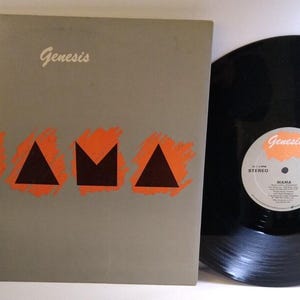 May include: A vinyl record album by Genesis, titled "Mama." The album cover is gray with the band's name in script and the word "MAMA" in orange and black block letters. The record is black with a white and orange label.