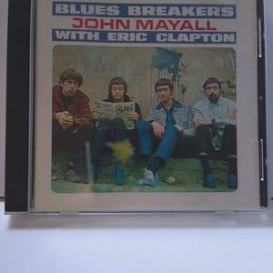 May include: CD case for the album "Blues Breakers" by John Mayall with Eric Clapton. The cover features a photograph of four men sitting outdoors. The album title and artist names are printed in blue and white.