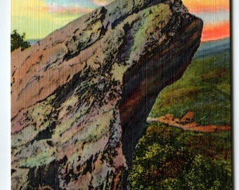 May include: Vintage postcard featuring Blowing Rock, North Carolina, with the text "301-Blowing Rock, Alt. 4000 Ft., Western North Carolina." The image shows a large rock formation against a backdrop of a colorful sky and green landscape. Pink flowers are in the foreground.