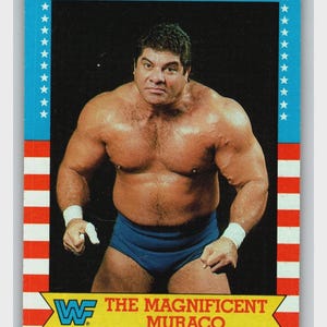 May include: A vintage wrestling trading card featuring a muscular man in blue trunks and white wristbands. The card has a red, white, and blue border with stars and stripes. Text reads "The Magnificent Muraco" and the WWF logo.