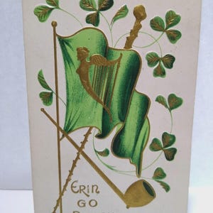 May include: Vintage postcard with a green flag featuring a golden harp and an angel, crossed poles, and a smoking pipe. The flag is surrounded by green shamrocks with gold accents. The text "Erin Go Bragh" is written in gold.