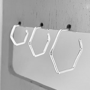 May include: Three silver hexagonal hoop earrings hanging on a display stand.