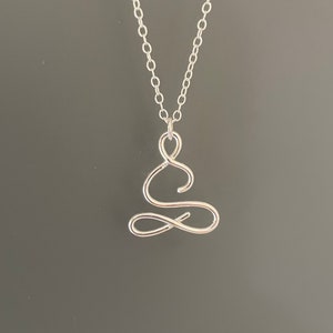 May include: A silver necklace featuring a delicate, wire-wrapped pendant shaped like a person in a seated meditation pose.
