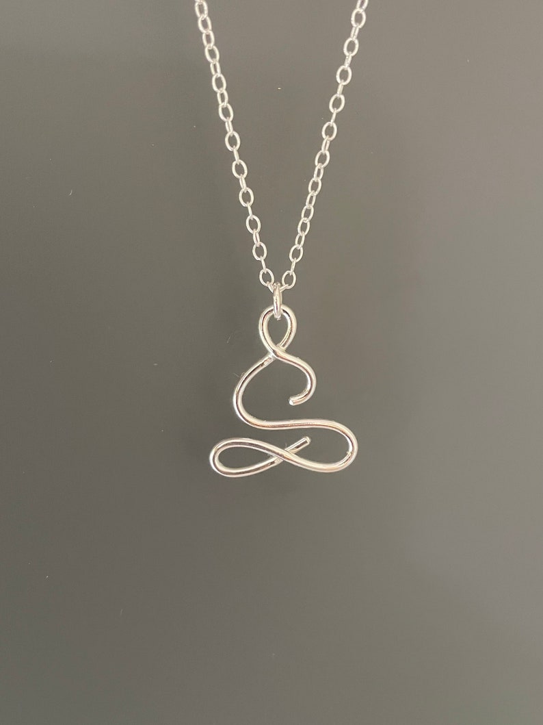May include: A silver necklace featuring a delicate, wire-wrapped pendant shaped like a person in a seated meditation pose.