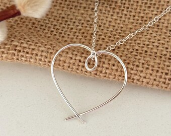 May include: A silver necklace with a simple, wire-wrapped heart pendant.
