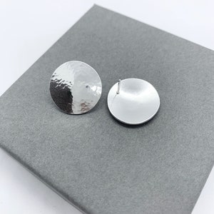 May include: A pair of silver stud earrings with a hammered texture. The earrings are round and have a smooth back.