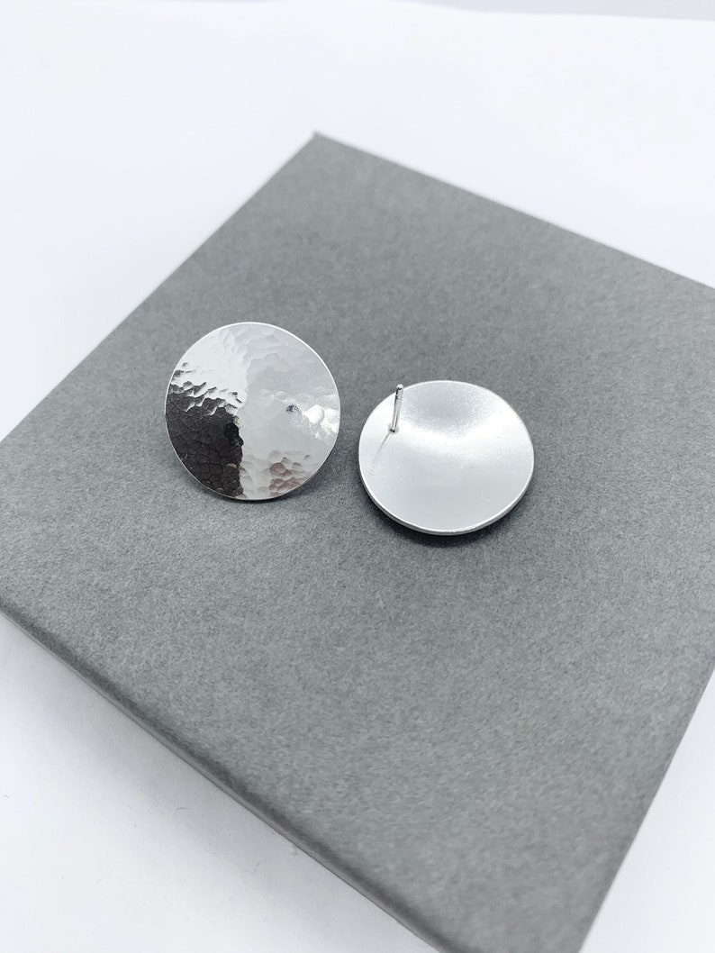May include: A pair of silver stud earrings with a hammered texture. The earrings are round and have a smooth back.