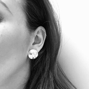 May include: A close-up of a person's ear with a silver hammered circle earring.