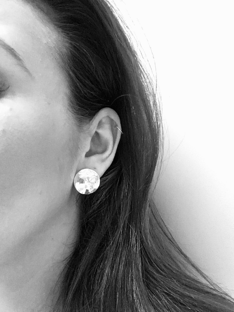 May include: A close-up of a person's ear with a silver hammered circle earring.
