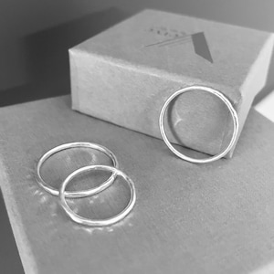 May include: Three silver rings on a brown box. The rings are simple and delicate, with a smooth, polished finish.