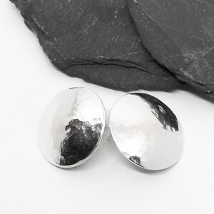 May include: A pair of silver hammered disc earrings. The earrings are round and have a textured surface.