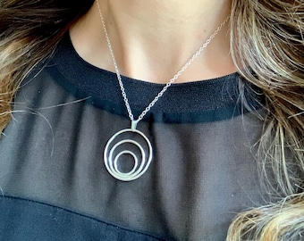 May include: A silver necklace with a pendant featuring three concentric circles. The circles are all connected and create a modern and minimalist design.