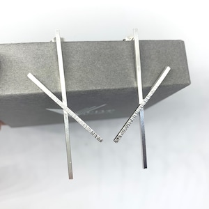 May include: A pair of silver earrings with a geometric design. Each earring features two straight bars that intersect at a right angle.