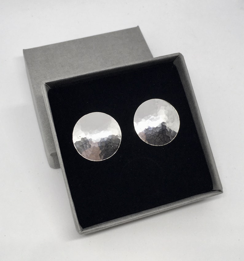 May include: A pair of silver hammered disc earrings in a gray gift box with a black interior.