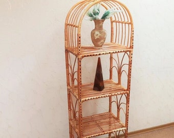 May include: A four-tiered, arched, natural wicker shelf unit with a vase and a cone-shaped object on the shelves.