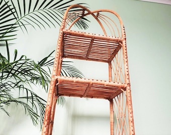 May include: A three-tiered wicker shelf unit with a natural brown finish. The shelf unit has a curved top and is made of woven rattan.