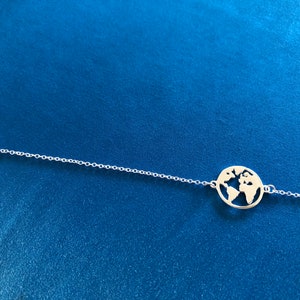 May include: A silver chain bracelet with a circular pendant featuring a cut-out design of the world.