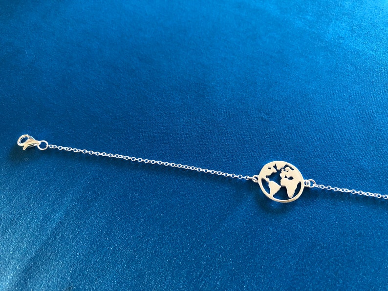 May include: A silver chain bracelet with a circular pendant featuring a cut-out design of the world.