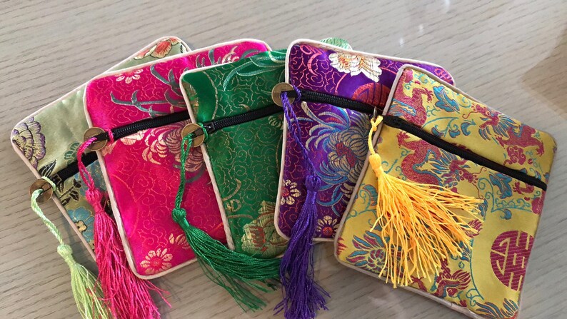 May include: Five small zippered pouches with tassels. The pouches are made of a colorful brocade fabric with floral and dragon designs. The pouches are lined with a cream-colored fabric.