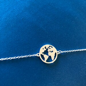 May include: A silver necklace with a delicate chain and a pendant shaped like the Earth. The pendant is cut out to show the continents.
