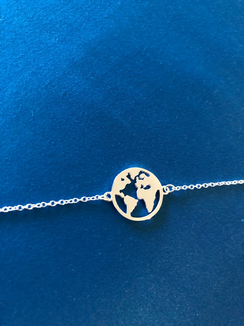 May include: A silver necklace with a delicate chain and a pendant shaped like the Earth. The pendant is cut out to show the continents.