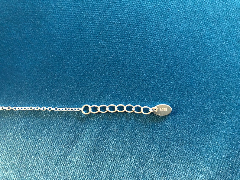May include: Close-up of a silver chain with a lobster clasp and a small oval tag that says "925".