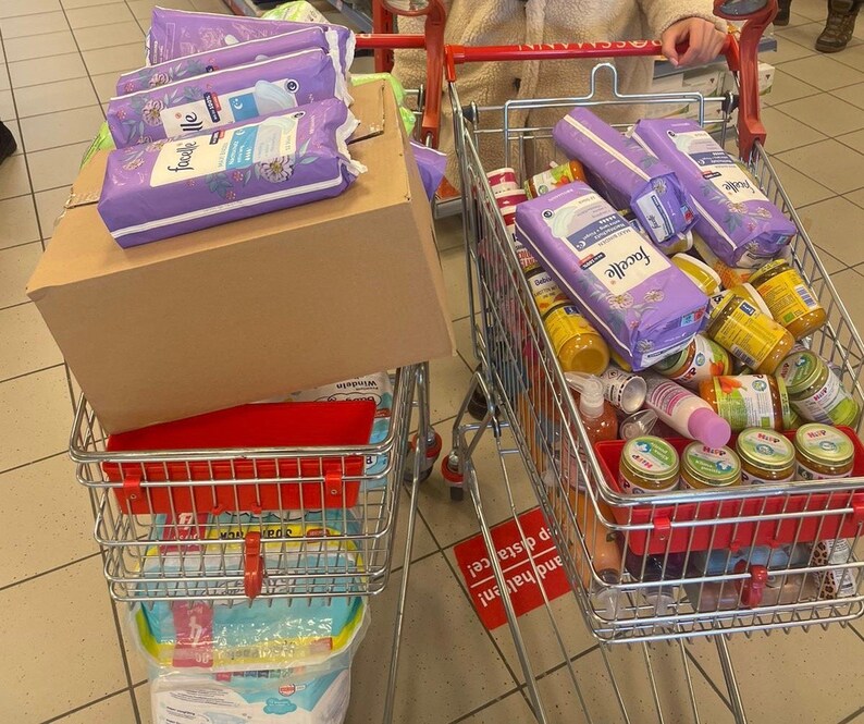 May include: Two shopping carts filled with various items. One cart contains a stack of purple and white boxes with the word "Facelle" printed on them. The other cart contains a variety of jars and bottles, including baby food jars and a few bottles of lotion.