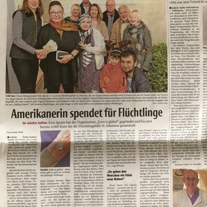 May include: A woman in a red sweater hands a stack of bills to a woman in a black jacket. The text in the image reads "Amerikanerin spendet f&uuml;r Fl&uuml;chtlinge" and "Love is global".