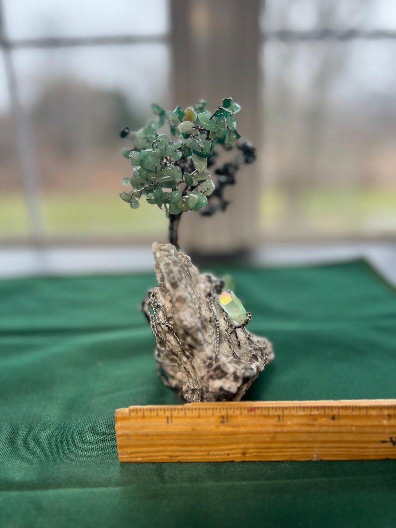 May include: A green gemstone wire wrapped tree sculpture on a rock base. The tree is made of wire and green gemstones. The base is made of a rough, gray rock.