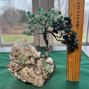 May include: A green crystal wire wrapped tree sculpture with a white crystal base. The tree is approximately 7 inches tall.