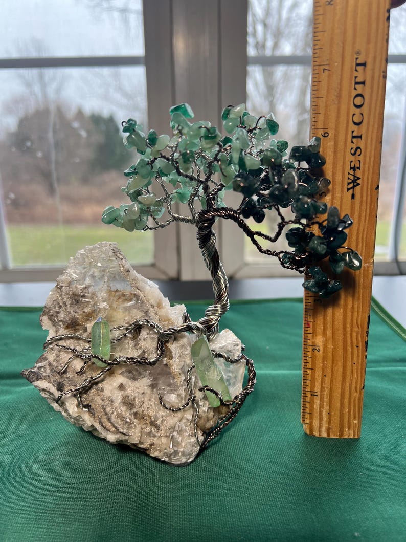 May include: A green crystal wire wrapped tree sculpture with a white crystal base. The tree is approximately 7 inches tall.