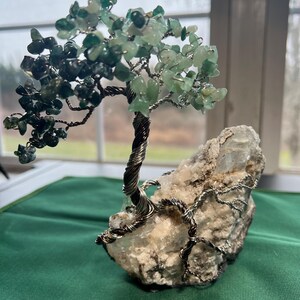 May include: A wire-wrapped tree made of green gemstones and silver wire, rooted in a white crystal rock. The tree is a decorative object, often used for home decor or as a gift.