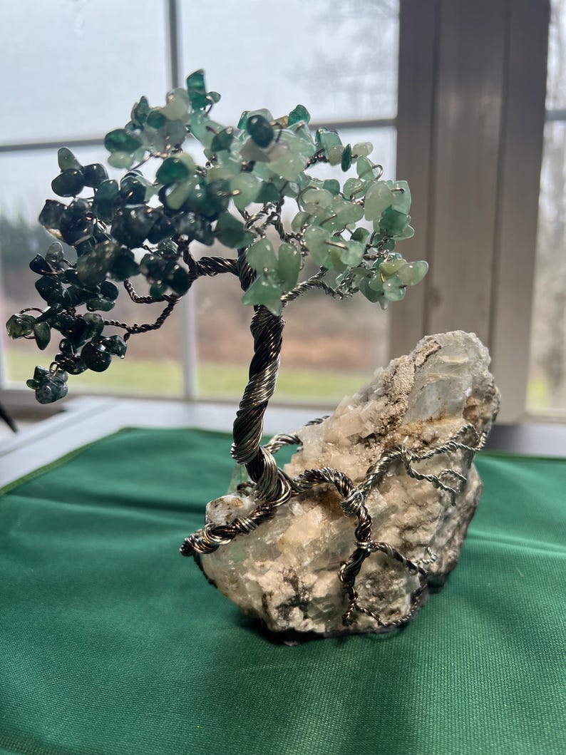 May include: A wire-wrapped tree made of green gemstones and silver wire, rooted in a white crystal rock. The tree is a decorative object, often used for home decor or as a gift.
