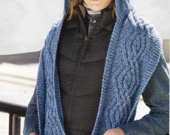 Peut inclure: Une écharpe à capuche en tricot bleu avec des détails en tricot torsadé et des poches. L'écharpe est portée par une personne avec un gilet noir et un jean bleu.