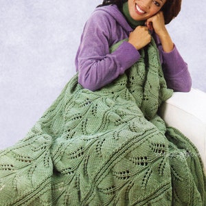 Puede incluir: Una manta de ganchillo verde con un patrón de hojas. La manta está drapeada sobre un sofá y una mujer está sentada en el sofá sosteniendo la manta.