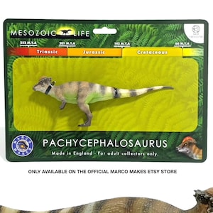 May include: A Pachycephalosaurus dinosaur figurine with a brown and tan patterned back, a light green underbelly, and a bony, domed head. The figure is displayed in front of its original rectangular packaging, which features Mesozoic Life branding.