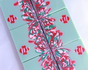 May include: Six rectangular bars of light green soap arranged in a grid. Each bar features a central vertical swirl pattern in red, white, and dark green, with small red and white bee-shaped embeds placed on the outer edges of the soap.